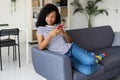 Smiling african american woman using mobile phone relaxing on sofa at home Royalty Free Stock Photo