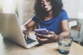 Smiling african american woman using smartphone and laptop while sitting at wooden table in the living room at home Royalty Free Stock Photo