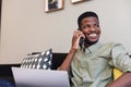 Smiling african american young businessman with laptop using smart phone on sofa in office Royalty Free Stock Photo