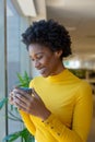 Smiling african american young female advisor with afro hairstyle holding coffee mug at workplace Royalty Free Stock Photo