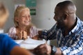 Smiling african american young male teacher looking at happy caucasian elementary schoolgirl at desk