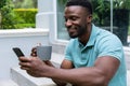 Smiling african american young man using smart phone while having coffee on steps outside house Royalty Free Stock Photo