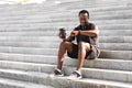 African Athete Guy Checking Fitness Tracker After Training Outdoors, Sitting On Steps Royalty Free Stock Photo