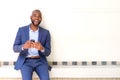 Smiling african business man sitting against wall with mobile phone Royalty Free Stock Photo