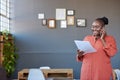 Smiling African businesswoman talking on a cellphone and reading paperwork