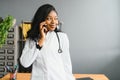 Smiling african female doctor physician holding cell phone talking on mobile at work. Healthcare professional answering Royalty Free Stock Photo