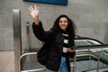 Smiling african girl using mobile phone and waving hand while standing by escalator Royalty Free Stock Photo