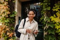 Smiling african girl listening music with headphones and drinking coffee while standing outdoors Royalty Free Stock Photo