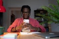 Smiling black guy holding smartphone chatting with girlfriend while studying at home in evening Royalty Free Stock Photo