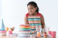 Smiling African little kid girl in cute dress, surprised on birthday party, looking at beautiful rainbow cake decorated with sugar Royalty Free Stock Photo