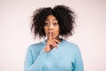 Smiling african woman with curly hair holding finger on her lips over white background. Gesture of shhh, secret, silence Royalty Free Stock Photo