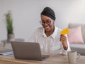Smiling african woman freelancer holding credit card, working online