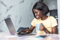 Smiling young african woman using laptop computer while sitting at home with cup of coffee Royalty Free Stock Photo
