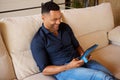 Smiling african young man sitting on sofa and using digital tablet at home Royalty Free Stock Photo
