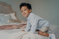 Smiling Afro American child trying to climb on big bed at home, having fun indoors Royalty Free Stock Photo