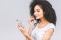 Smiling afro american woman applying makeup powder with brush isolated on a grey background. Using phone Royalty Free Stock Photo