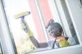 Smiling young afro american woman cleaning glass window with squeegee Royalty Free Stock Photo
