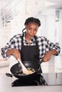 Smiling afro american woman holding a deep frying pan and stirring eggs