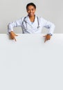 Smiling afro female intern doctor pointing at blank advertisement board Royalty Free Stock Photo