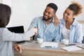 Smiling afro spouses handshaking with insurance broker in office