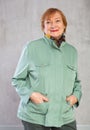 Smiling aged woman in green jacket with hands in pockets Royalty Free Stock Photo