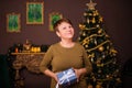 Smiling aged woman holding a gift in her hands while standing against the background of the Christmas interior and Christmas tree Royalty Free Stock Photo