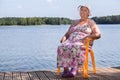 Smiling aged woman sitting on wooden pier at lake, copyspace Royalty Free Stock Photo