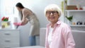Smiling aged woman looking at camera, housekeeper wiping dust in room, cleaning Royalty Free Stock Photo