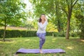 The smiling and amazing woman is practicing yoga in the green grass. A lady is good-looking and doing sports exercise in the park.