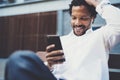 Smiling american african man using smartphone to listen to music while sitting on the bench at sunny street.Concept of Royalty Free Stock Photo