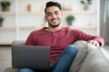 Smiling arab guy reclining on sofa with laptop