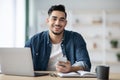 Smiling arab guy using smartphone while sitting at workdesk Royalty Free Stock Photo