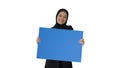 Smiling Arab woman in hijab holding blank blue poster and lookin Royalty Free Stock Photo