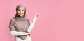 Smiling arabian girl pointing at copy space over pink background