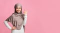 Smiling arabic girl in headscarf showing ok sign on pink background