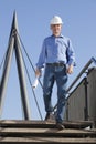 Smiling architect or engineer with hard hat and blueprint in his hand walking downstairs at a construction site Royalty Free Stock Photo