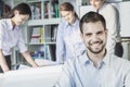 Smiling architect looking at camera while colleagues are planning around a table and looking at a blueprint Royalty Free Stock Photo