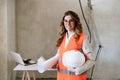 Smiling architect woman in construction site holding blueprints and helmet. Home renovation