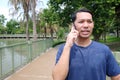 Smiling Asain man talking with smartphone in the park. Technology and lifestyle.