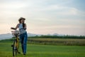 Smiling Asia woman with bicycling at the garden meadow in sunset near mountain background.