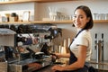 Smiling asian barista girl makes cappuccino with coffee machine, stands behind counter in cafe Royalty Free Stock Photo