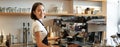 Smiling asian barista girl makes cappuccino with coffee machine, stands behind counter in cafe Royalty Free Stock Photo