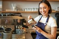 Smiling asian barista girl, making coffee, pouring steamed milk into cappuccino, doing latte art in cup, working in cafe Royalty Free Stock Photo