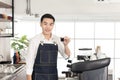 Smiling Asian barista man show cup of black coffee, feeling happy look at camera in coffee shop