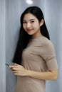 Smiling asian beautiful woman Standing wearing a Gray dress holding smartphone  in the bedroom behind a curtain. Female asia smlie Royalty Free Stock Photo