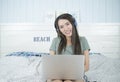 Smiling asian beauty woman sitting on the bed listening music from headphone and playing notebook computer on bed. Royalty Free Stock Photo