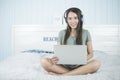 Smiling asian beauty woman sitting on the bed listening music from headphone and playing notebook computer on bed. Royalty Free Stock Photo