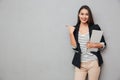 Smiling asian business woman holding laptop computer and pointing away