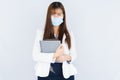 Smiling Asian business woman wearing a medical face mask holding the notebook and looking at the camera over grey background. Back Royalty Free Stock Photo