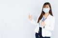 Smiling Asian business woman wearing a medical face mask and pointing finger to side blank space over grey background. Back to the Royalty Free Stock Photo